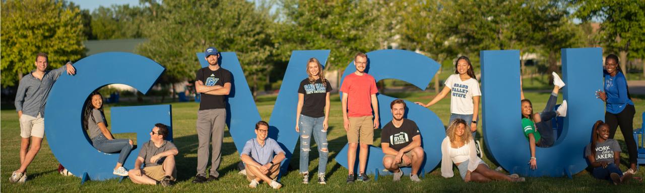 Students pose with the bright blue "GVSU" letters in front of the Cook Carillon Clock Tower on Grand Valley State Unviersity's Allendale Campus.